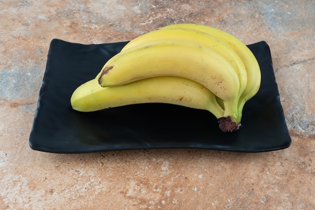 Un plato oscuro lleno de plátanos de frutas maduras en el cuadro gris.