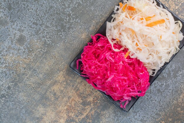 Un plato oscuro lleno de repollo rojo salado sobre fondo de mármol. Foto de alta calidad