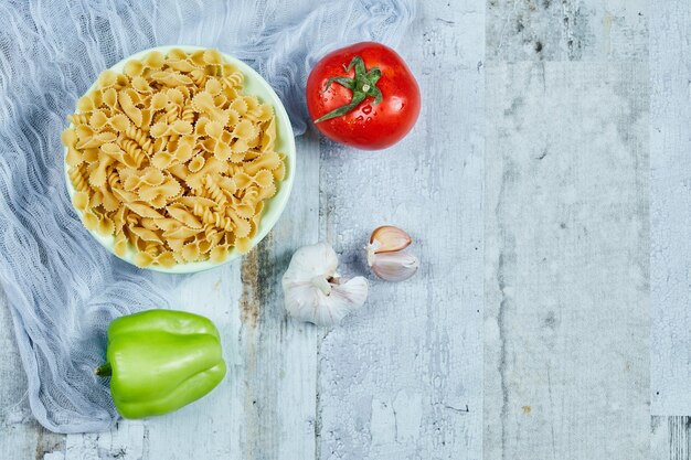 Un plato de pasta cruda con tomate, pimiento y ajo.