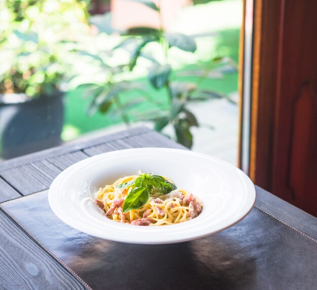 Plato de pasta de espaguetis con hojas de albahaca sobre mantel sobre la mesa