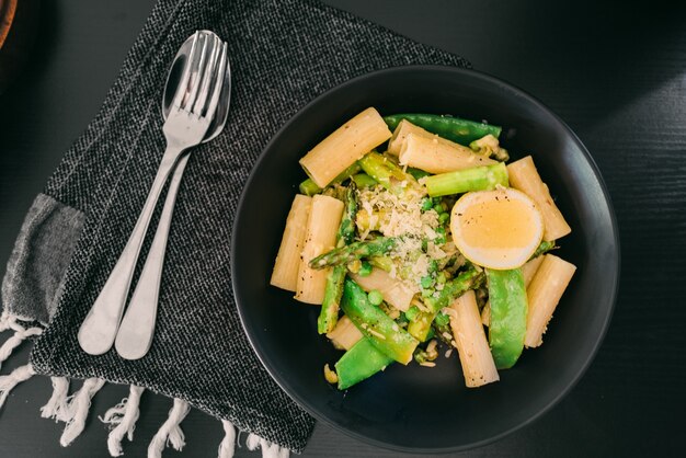 Plato con pasta, espárragos y huevo sobre una mesa negra