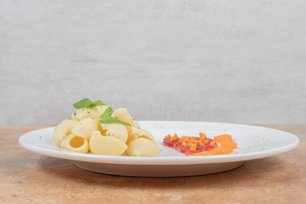 Plato de pasta en forma de concha con salsa en espacio de mármol.