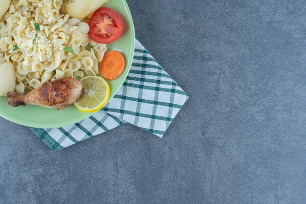 Plato de pasta hervida y muslo de pollo sobre la superficie de piedra.