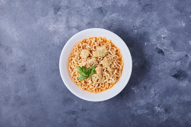 Un plato de pasta en el medio de la mesa azul con hierbas.