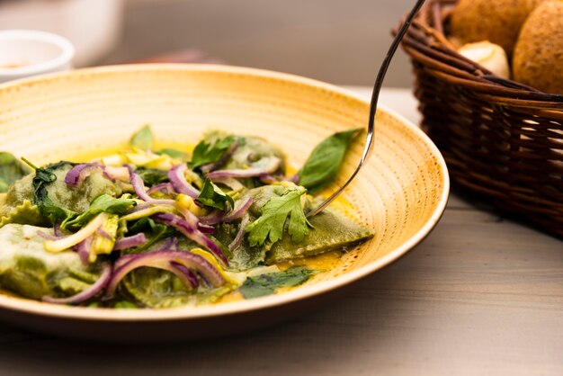 Plato de pasta de ravioles verdes con hojas de cebolla y cilantro