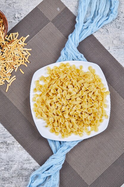 Un plato de pastas crudas con mantel azul sobre mesa de mármol.