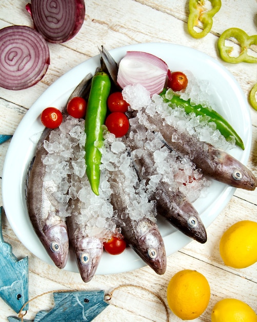 Plato de pescado crudo cubierto con pimiento, tomate cherry y cebolla roja