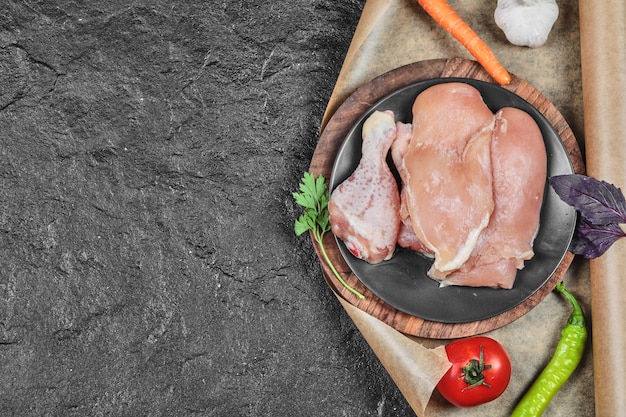 Plato de piezas de pollo crudo con tomate y zanahoria sobre superficie oscura