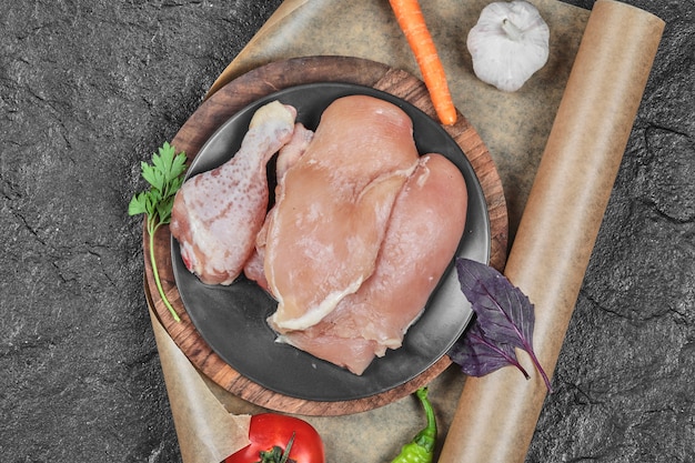 Plato de piezas de pollo crudo con tomate y zanahoria sobre superficie oscura