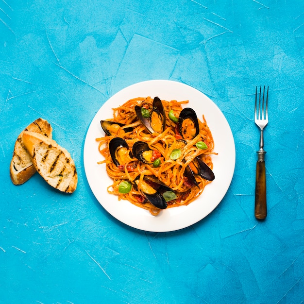 Plato plano de pasta con mejillones y tenedor.