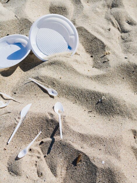 Plato de plástico blanco y cuchara sobre arena en la playa