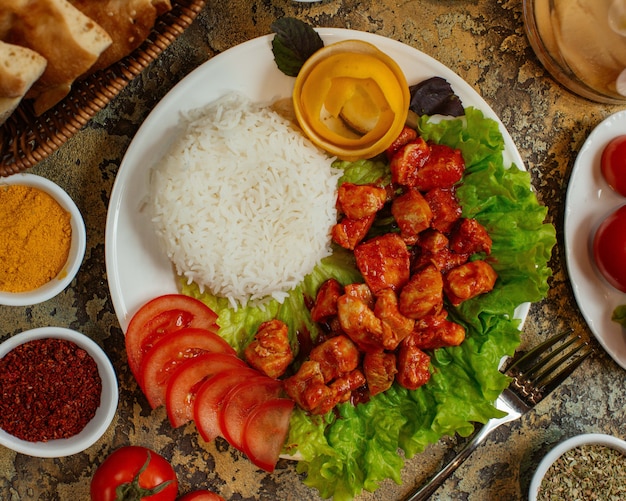 Plato de pollo con trozos de pollo en salsa de tomate servido con arroz y tomates.