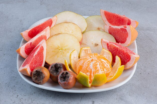 Un plato de pomelos en rodajas, peras y una mandarina pelada sobre fondo de mármol.
