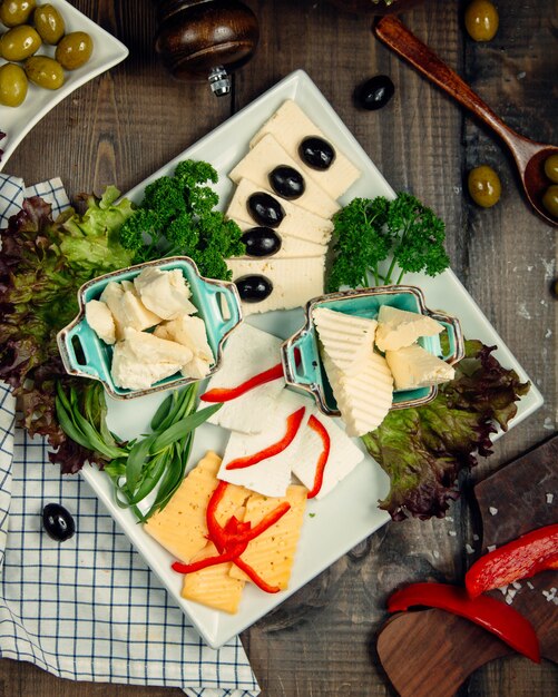 Plato de queso con aceitunas y hierbas verdes.