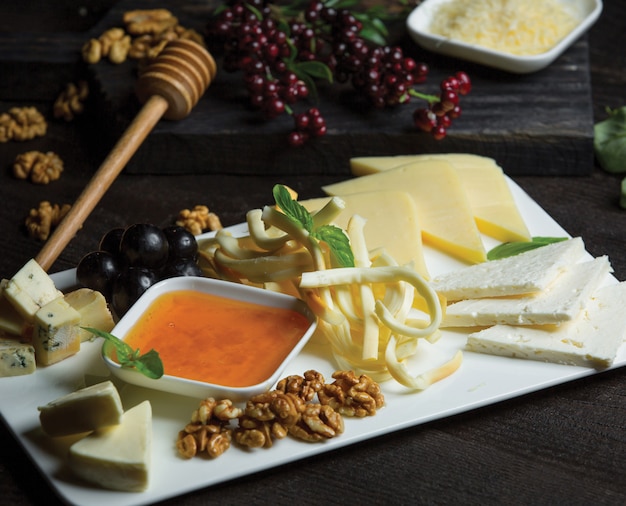 Plato de queso blanco de cerámica con diferentes tipos de queso, nueces y miel.