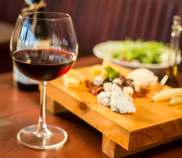 Foto gratuita plato de queso con una copa de vino tinto