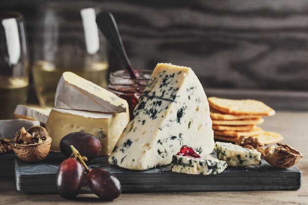 Plato de queso con diferentes artes de uva de queso y nueces servido en tablero de madera.