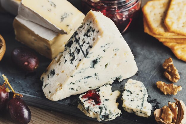 Plato de queso con diferentes artes de uva de queso y nueces servido en tablero de madera.