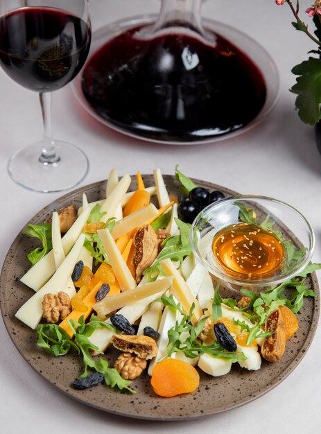 Plato de queso con nueces pasas rúcula aceitunas y copa de vino