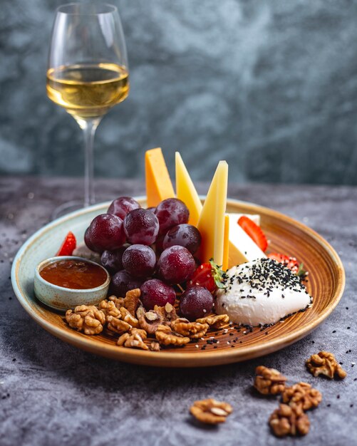 Plato de queso con nueces, uvas cheddar, queso de cabra, mozzarella, queso azul y fresas servidas con vino blanco.