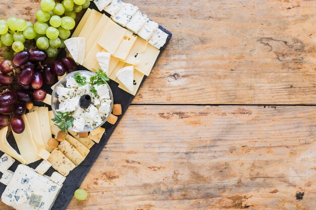 Plato de queso con uvas en tablero de pizarra negro sobre la mesa