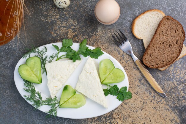 Plato de queso con verduras y rebanadas de pan.