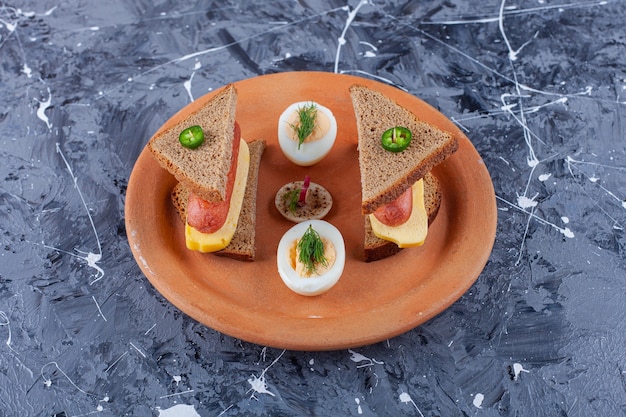 Plato de rebanadas de pan negro con queso y tomates sobre superficie de mármol.