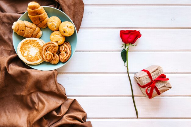 Plato con repostería cerca de rosa y presente