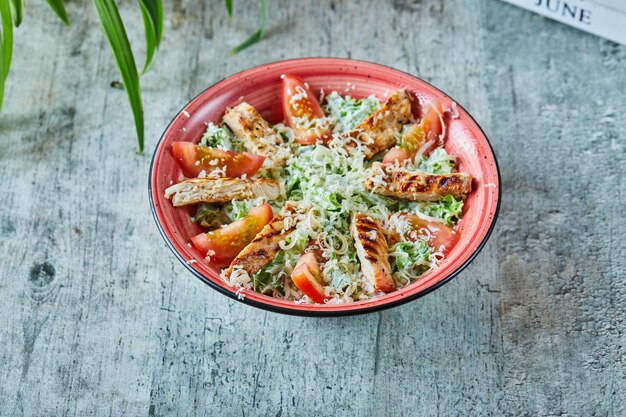 Un plato rojo con ensalada César y tomates en la superficie de mármol