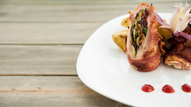 Foto gratuita plato con rollo de carne asada y trozos de papa en mesa de madera