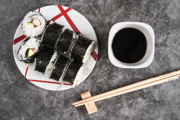 Plato con rollos de sushi junto a salsa de soja y palillos.