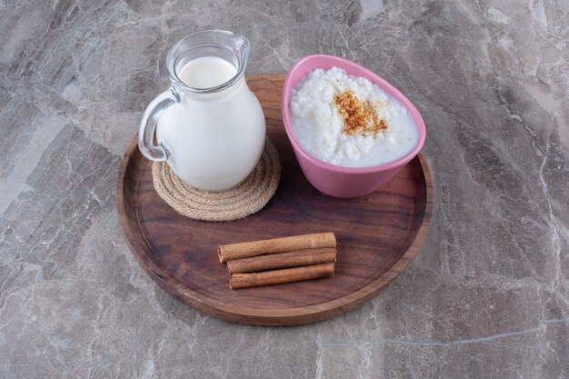 Un plato rosa de gachas de avena saludables con una jarra de vidrio de leche y palitos de canela sobre una tabla de madera.