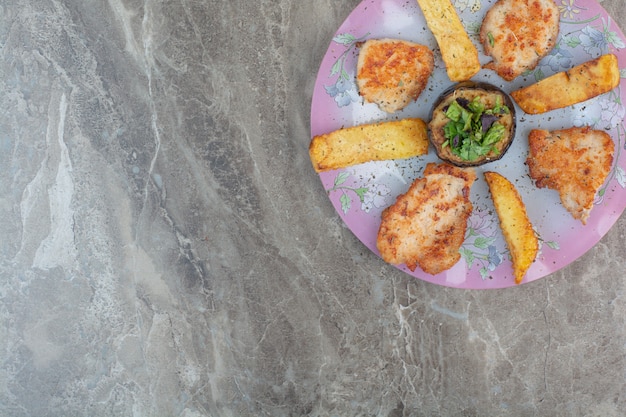 Un plato rosa lleno de pollo frito y patatas con berenjena.