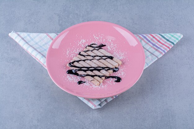 Un plato rosa de palos dulces con jarabe de chocolate y azúcar en polvo.