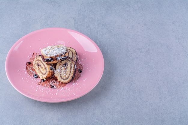 Un plato rosa de panecillo dulce en rodajas con jarabe de chocolate.