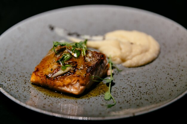 Plato de sabroso filete de salmón con salsa y puré en restaurante de comida moderna.