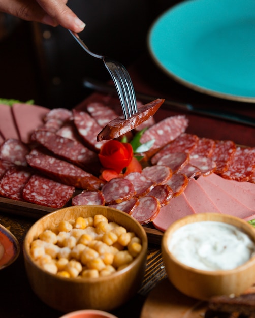 Foto gratuita plato de salami con rodajas de salchicha derivado con salados, salsa sobre tabla de madera