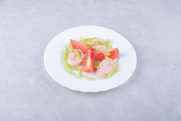 Foto gratuita plato de salchichas en rodajas y tomates sobre fondo de piedra.