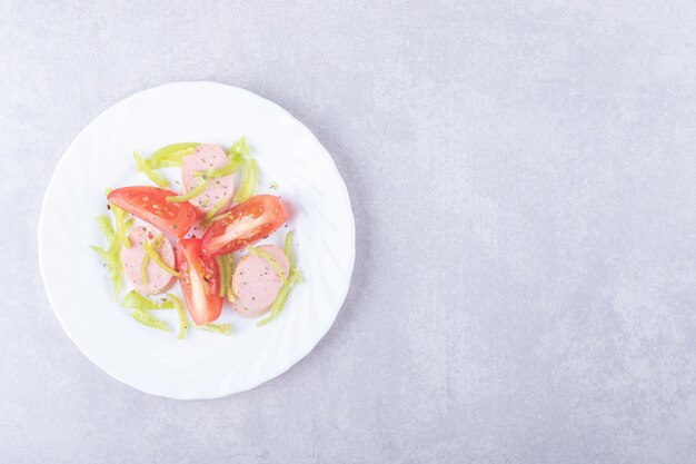 Plato de salchichas en rodajas y tomates sobre fondo de piedra.