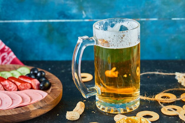 Un plato de salchichas y un vaso de cerveza en la mesa oscura.