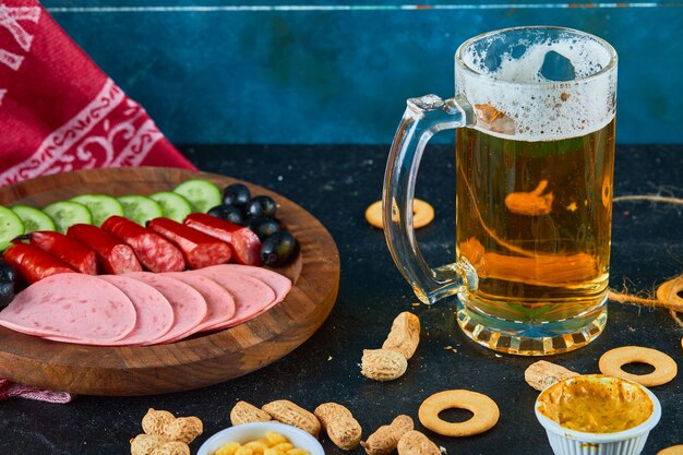 Un plato de salchichas y un vaso de cerveza en la mesa oscura.