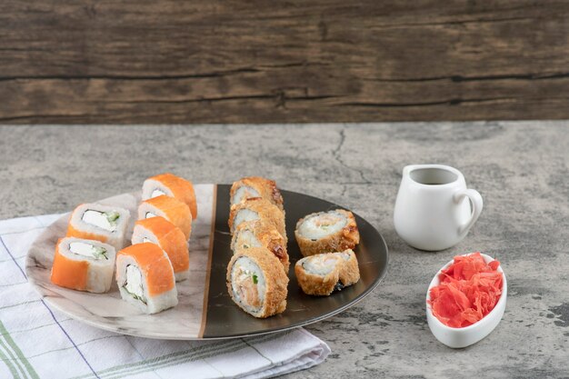 Plato de salmón y rollos de sushi caliente con jengibre encurtido sobre mesa de mármol