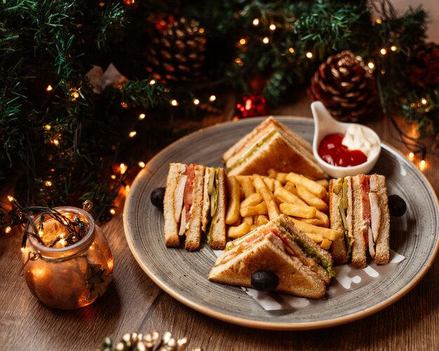 Un plato de sándwich club servido con papas fritas, mayonesa y salsa de tomate