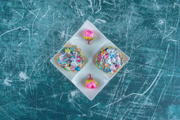 Un plato de servir con cupcakes y corolas de flores sobre fondo azul. Foto de alta calidad