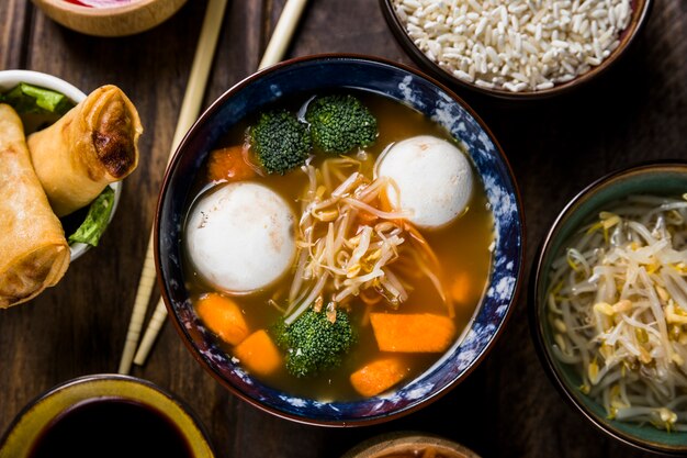 Plato de sopa de fideos clara con bola de pescado y vegetales en el escritorio de madera