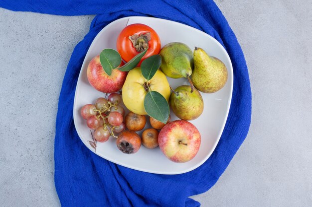 Plato de surtido de frutas apetitosas sobre mantel azul sobre fondo de mármol.