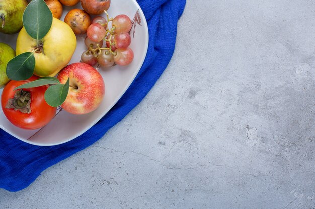 Plato de surtido de frutas apetitosas sobre mantel azul sobre fondo de mármol.