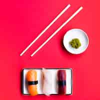 Foto gratuita plato de sushi con palitos de wasabi y chop sobre un fondo rojo.