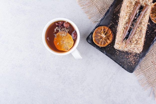 Plato de tarta casera con té de frutas sobre superficie de mármol.