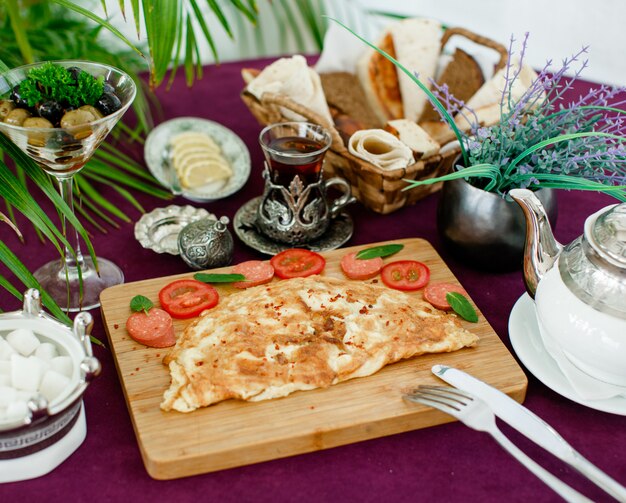 Plato de tortilla con salchichas y tomates, servido con té, aceitunas, pan y limón.